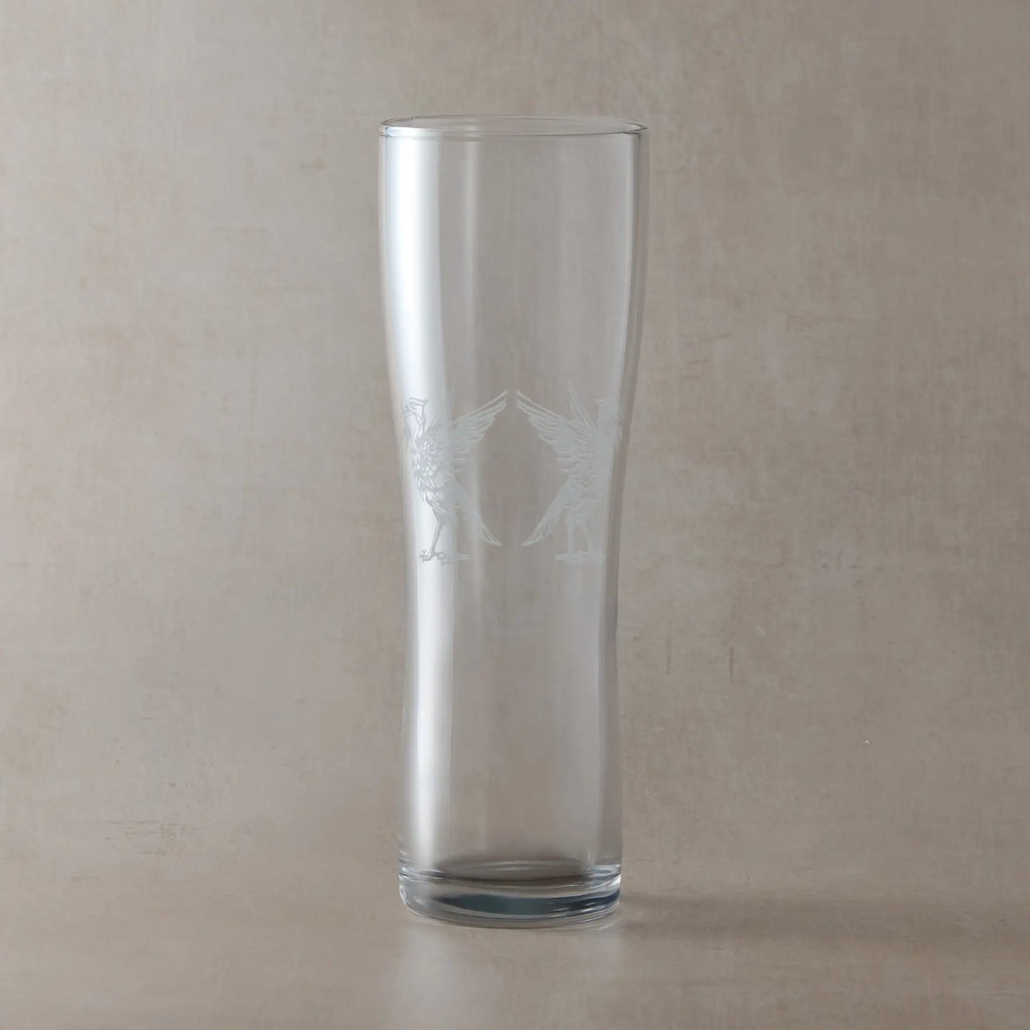 Tall pint glass with an engraving of two Liverbirds on a beige background