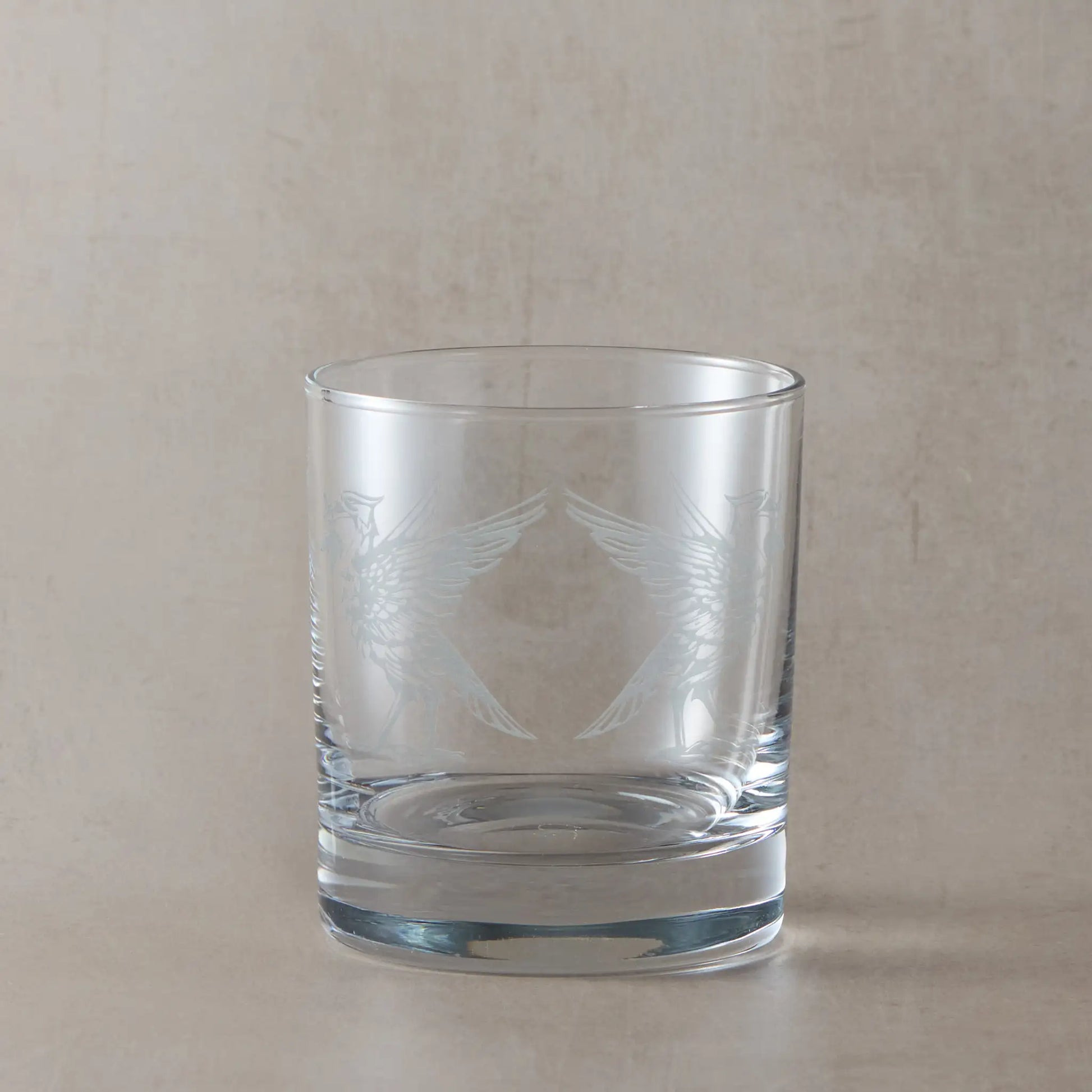 Whisky glass engraved with two Liverbirds, photographed on a beige background