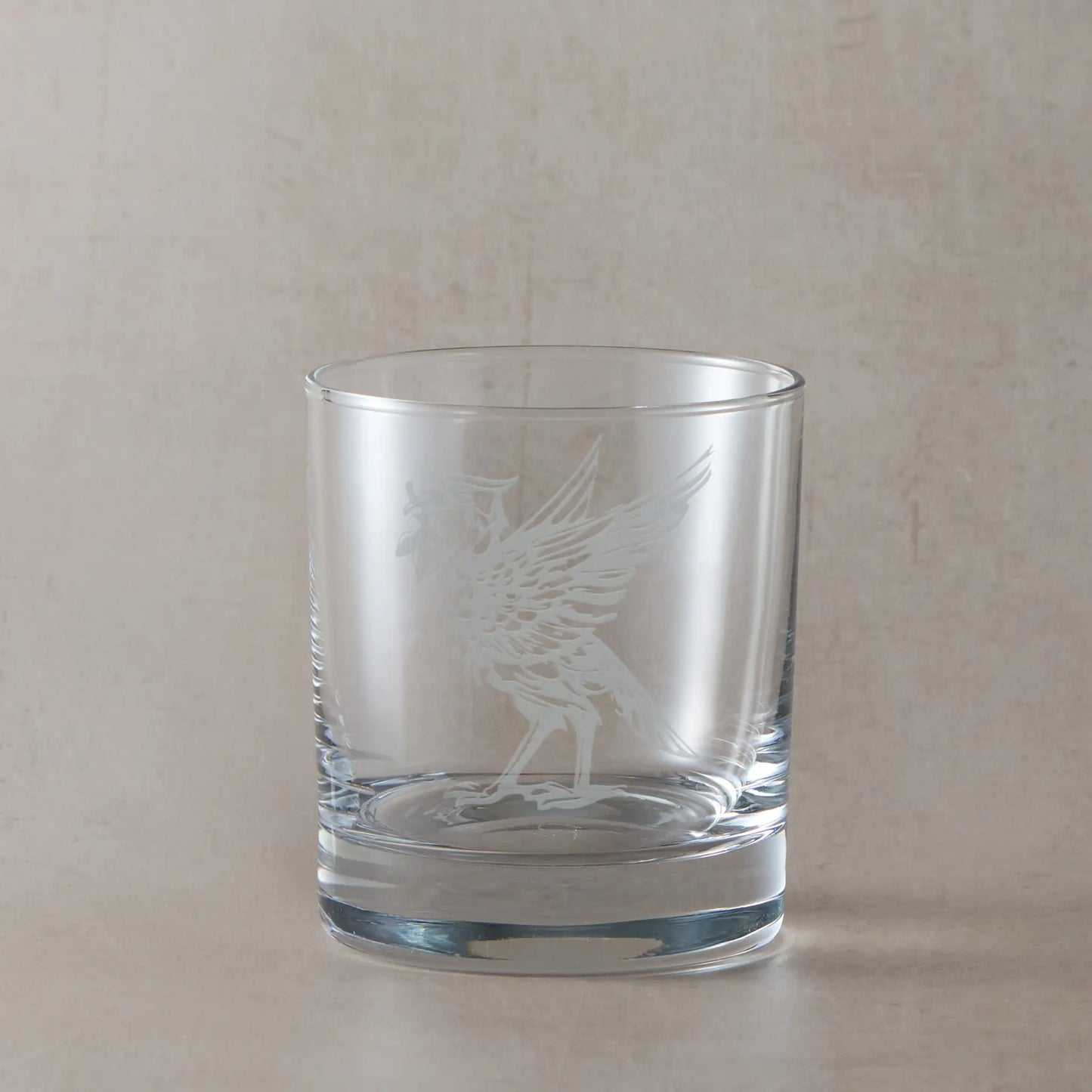 Whisky glass engraved with two Liverbirds, photographed on a beige background