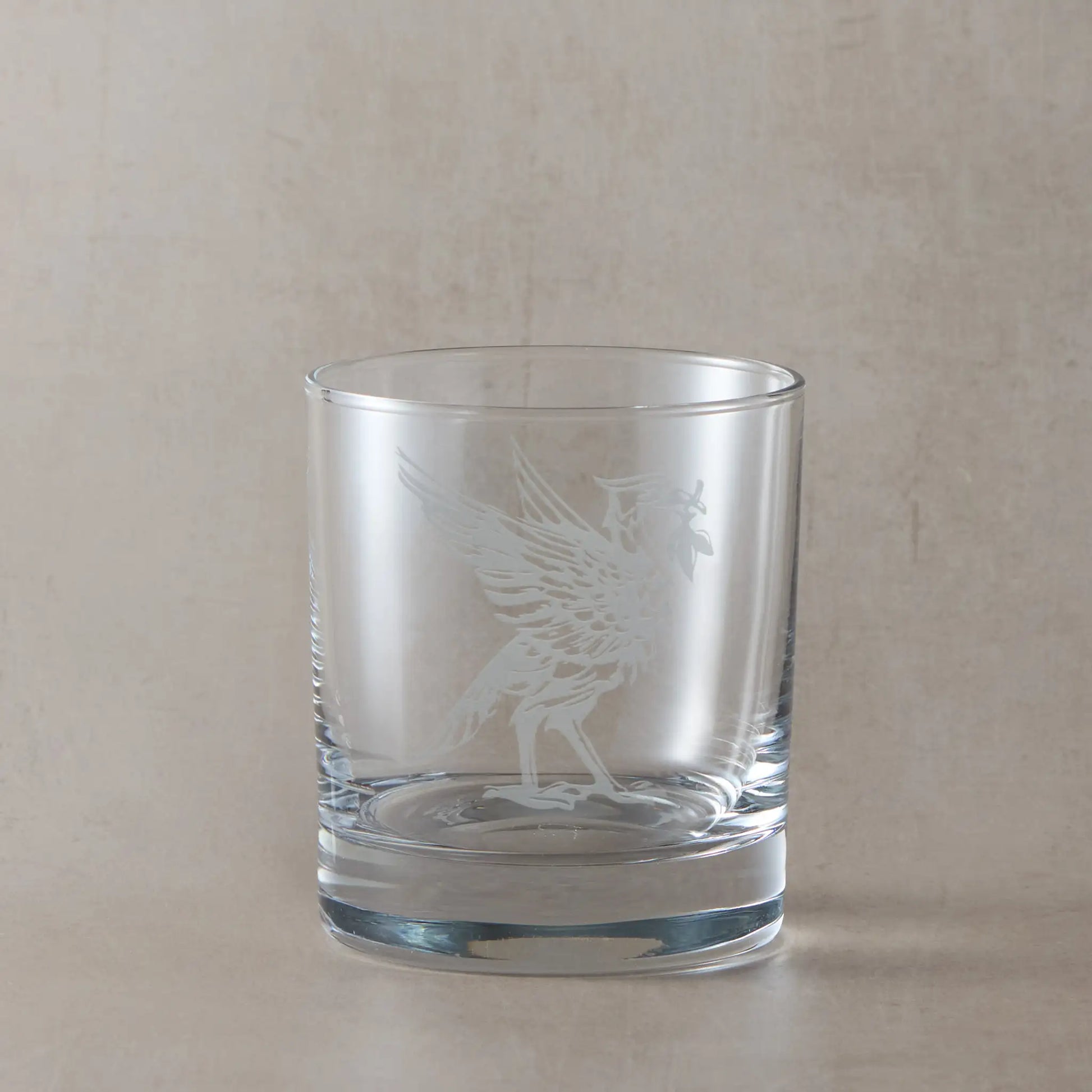 Whisky glass engraved with a Liverbird facing right photographed on a beige background