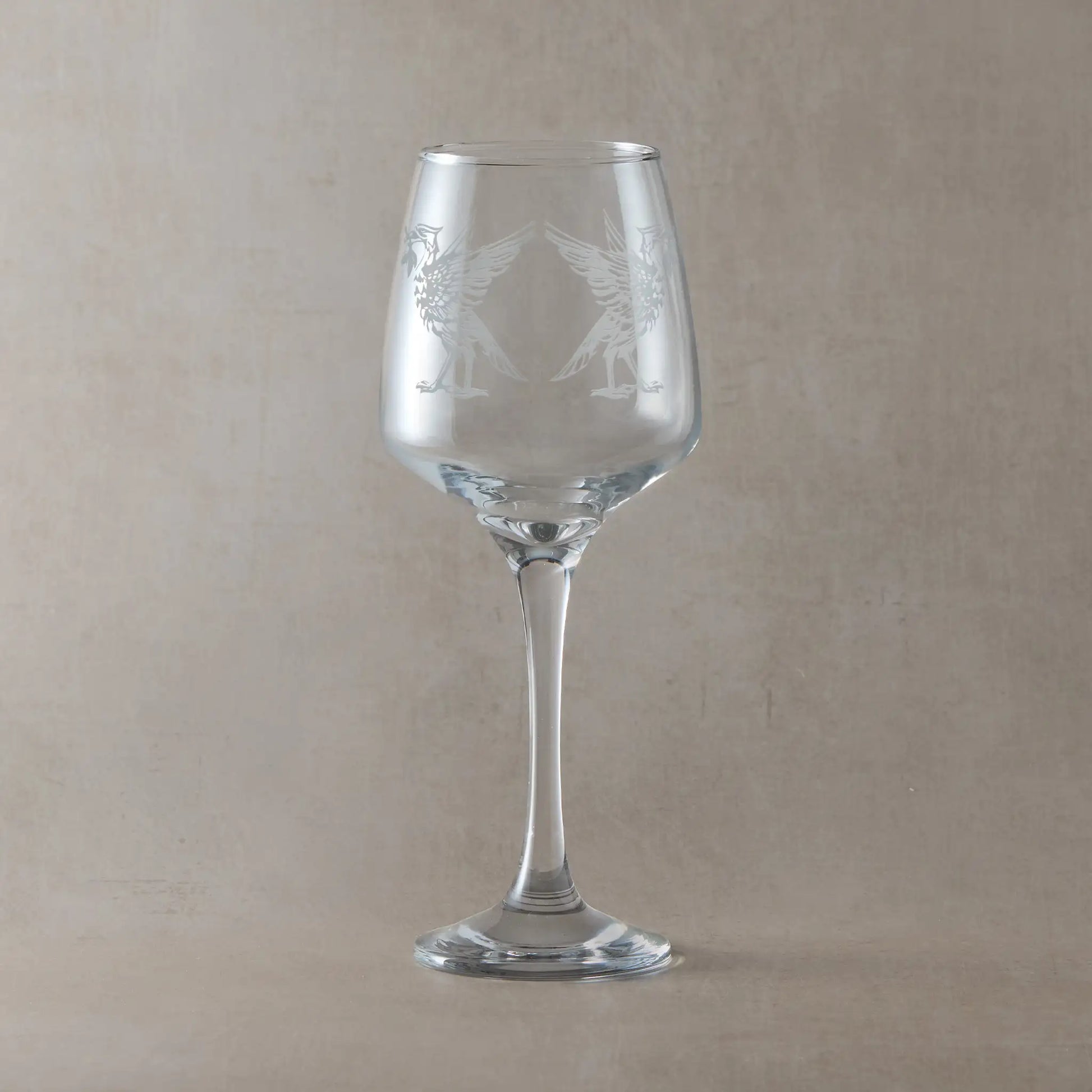 Clear wine glass engraved with two liverbirds, photographed on a light background
