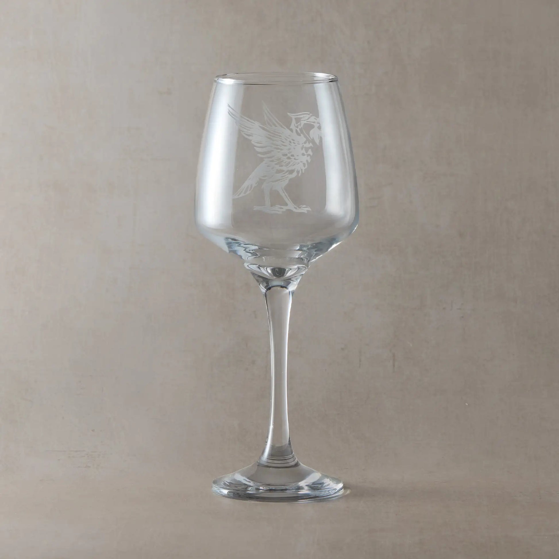 Wine glass engraved with a Liverird facing right, photographed on a natural background.