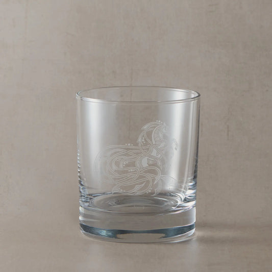 Engraved whisky glass featuring an intricate Celtic horse design, sandblasted onto clear glass against a neutral beige studio background