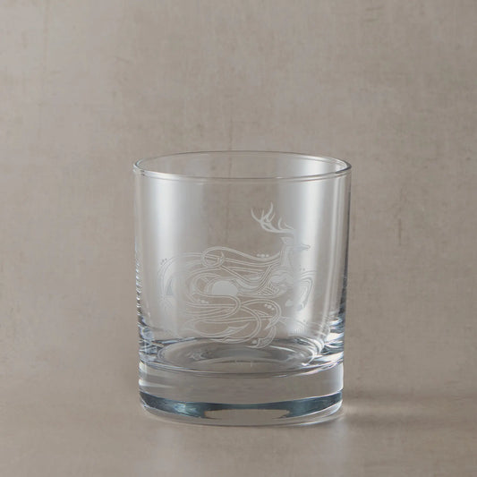 Engraved whisky glass featuring an intricate Celtic stag design, sandblasted onto clear glass against a neutral beige studio background
