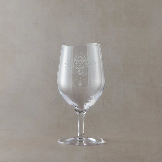 Clear wine glass with an engraved lotus flowe, om symbol and moon phases design on a beige background