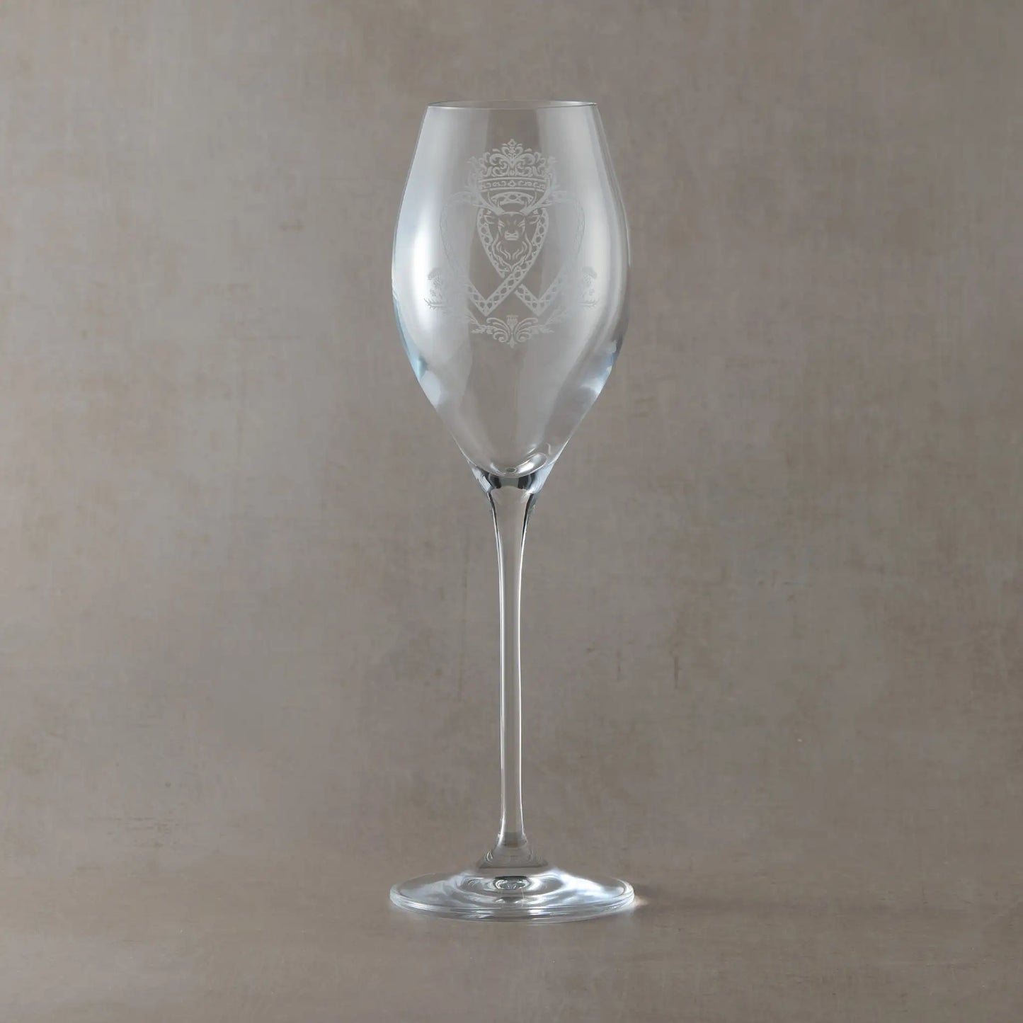Atelier prosecco glass engraved with crowned Luckenbooth, thistles, and stag design, shown on beige background