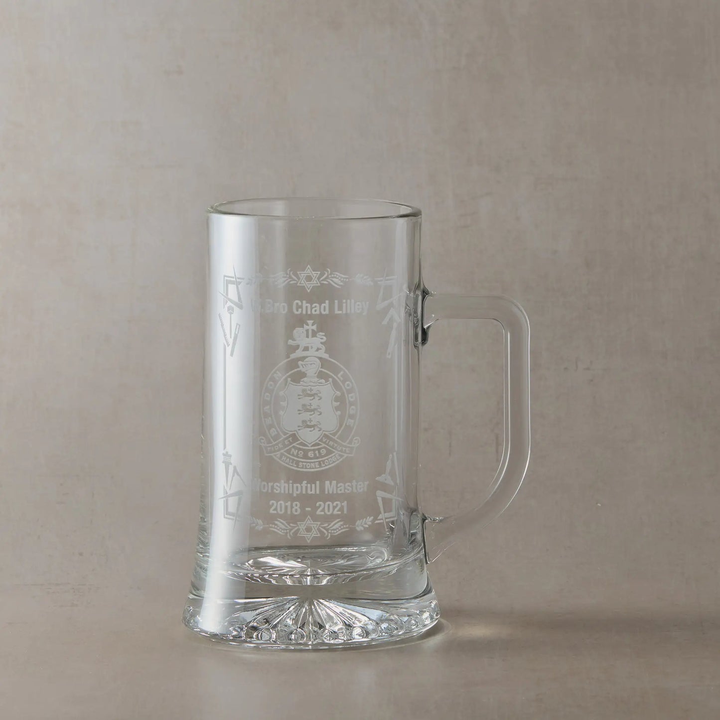 Engraved Masonic lodge crest tankard with right-handled glass, personalised with Worshipful Master name and dates, shown on a neutral beige studio background