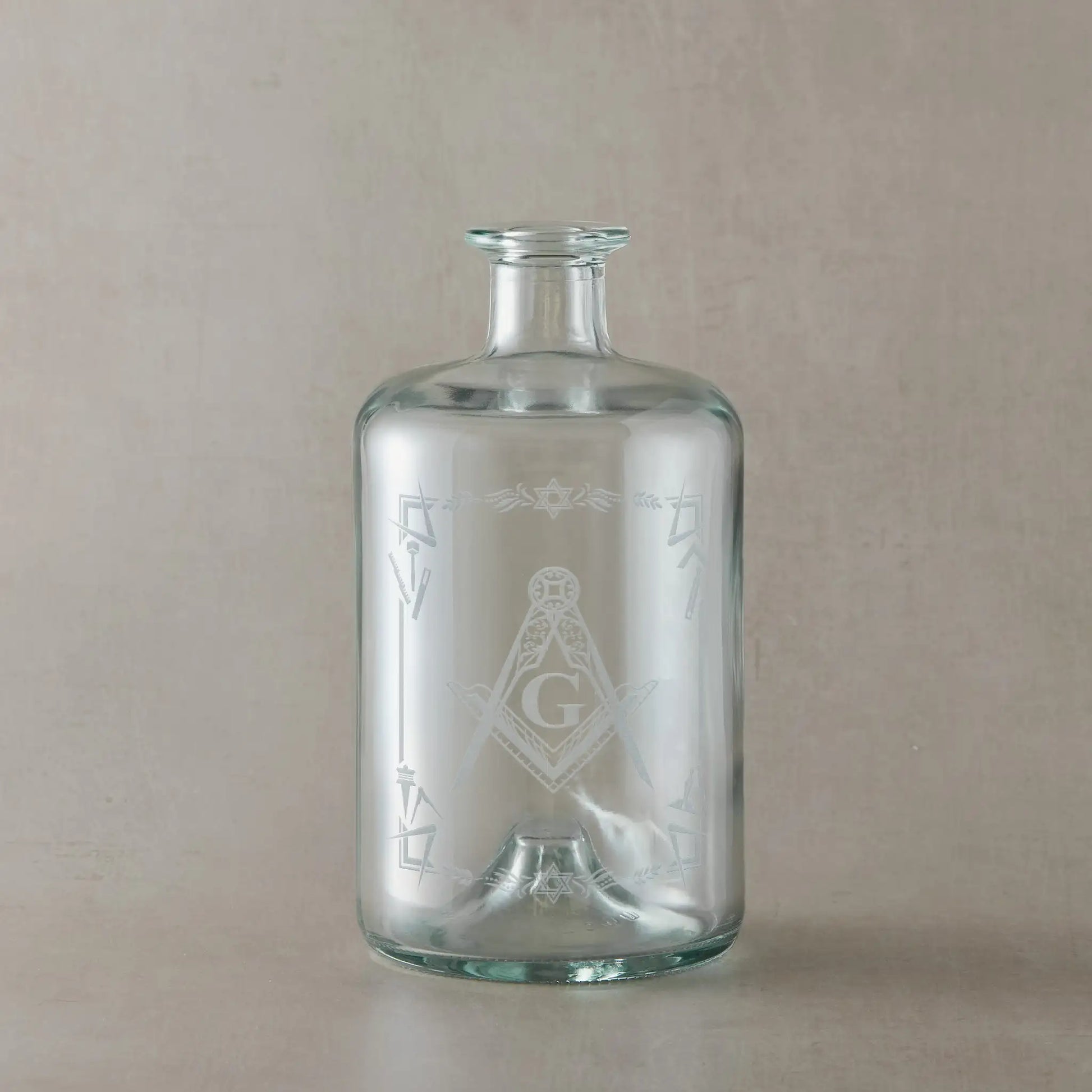 Apothecary style decanter engraved with masonic square and compass with G, shown on a beige background