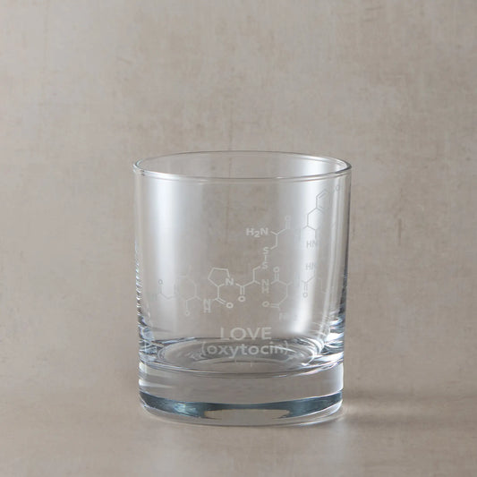 Whisky glass engraved with oxytocin molocules and the word Love, photographed on a beige background