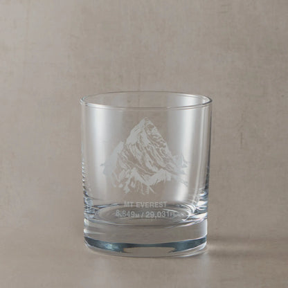 Clear whisky glass engraved with Mount Everest and its height in metres and feet, photographed on a soft neutral background

