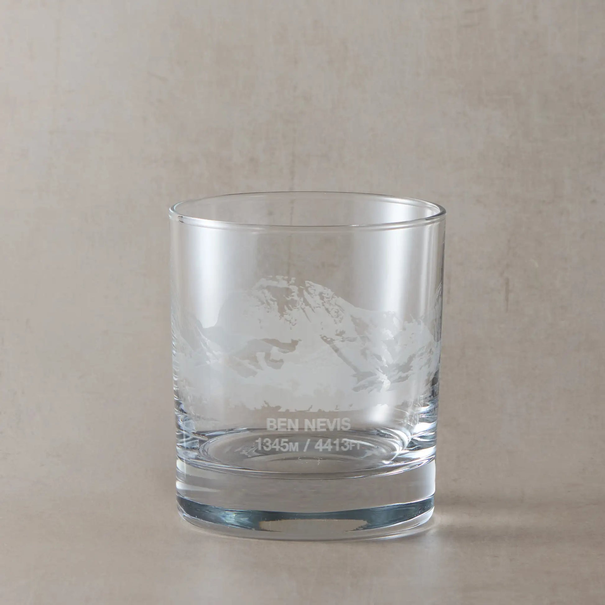 Whisky glass engraved with Ben Nevis, Scafell Pike and Snowdon, photographed on a studio background