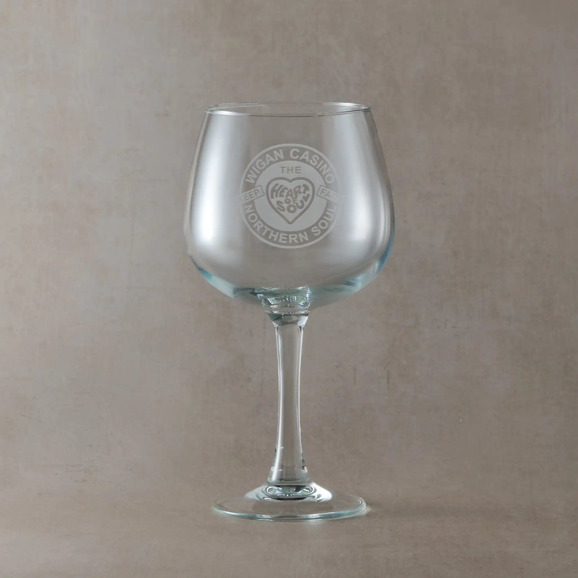 Gin glass engraved with a Wigan Casino badge and the words Keep the faith, heart and soul, on a beige background