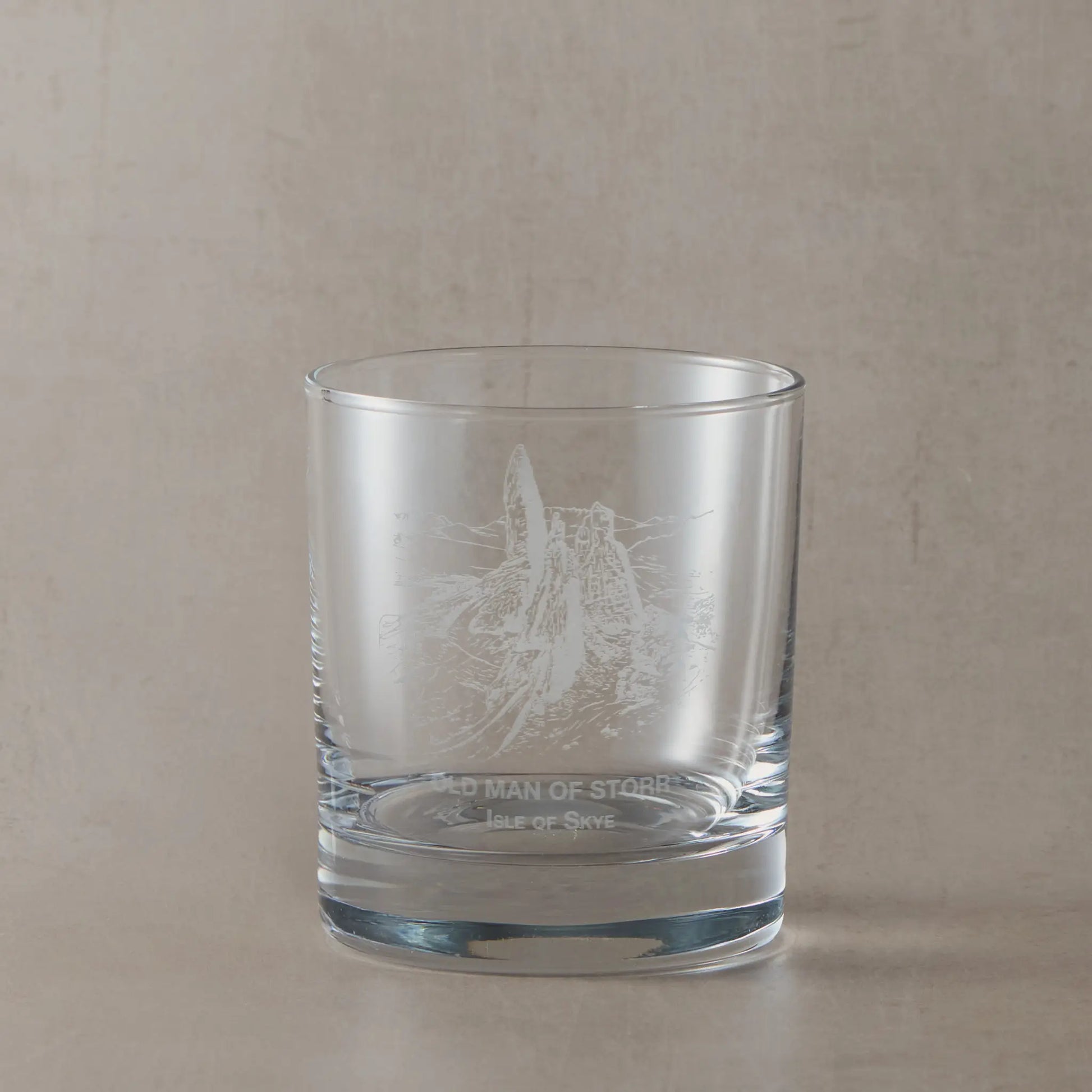 Clear whisky glass engraved with the Old Man of Storr rock formation on a soft neutral beige background