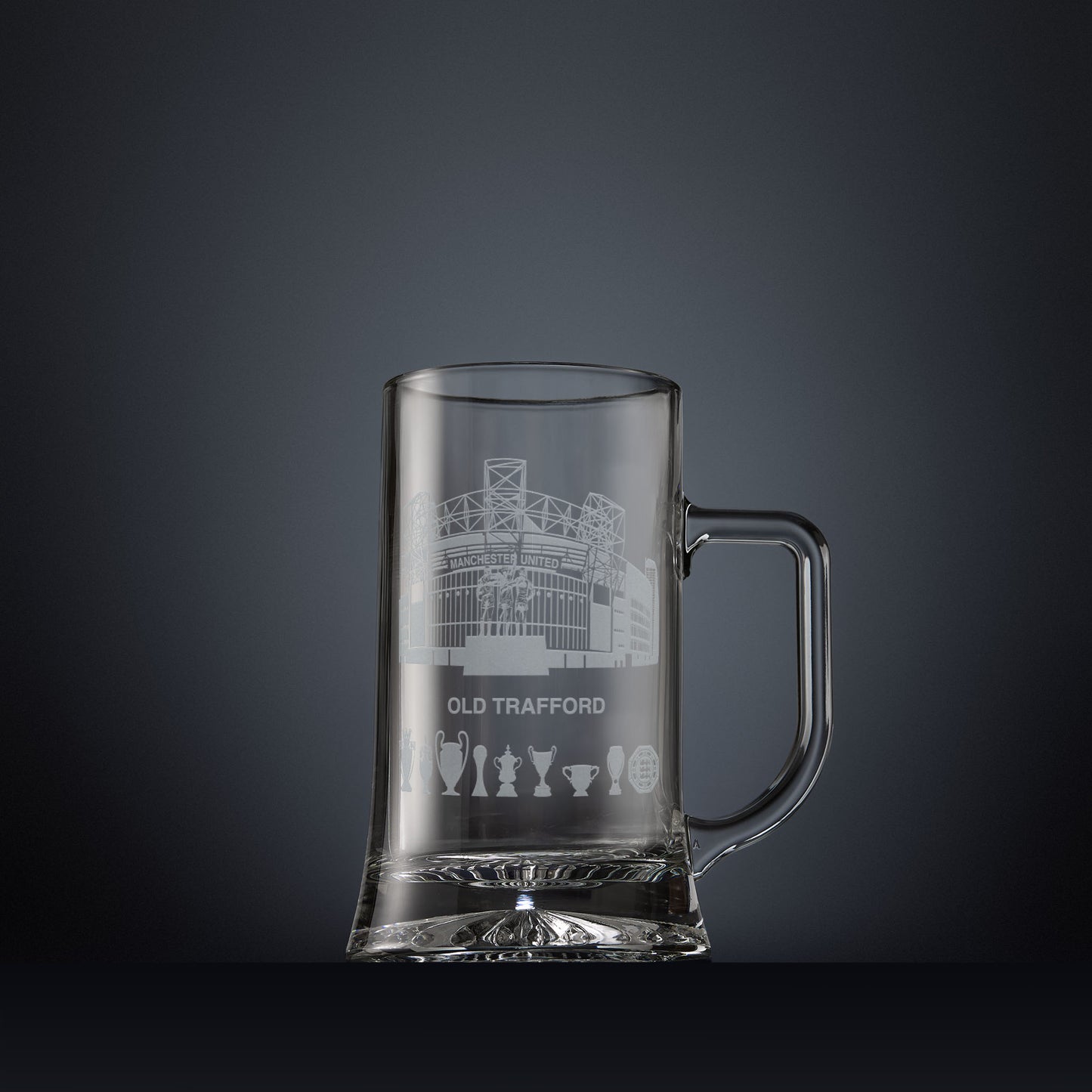 Glass tankard engraved with a line-art interpretation of Old Trafford stadium, with football trophy silhouettes beneath, inspired by its distinctive architectural form.
