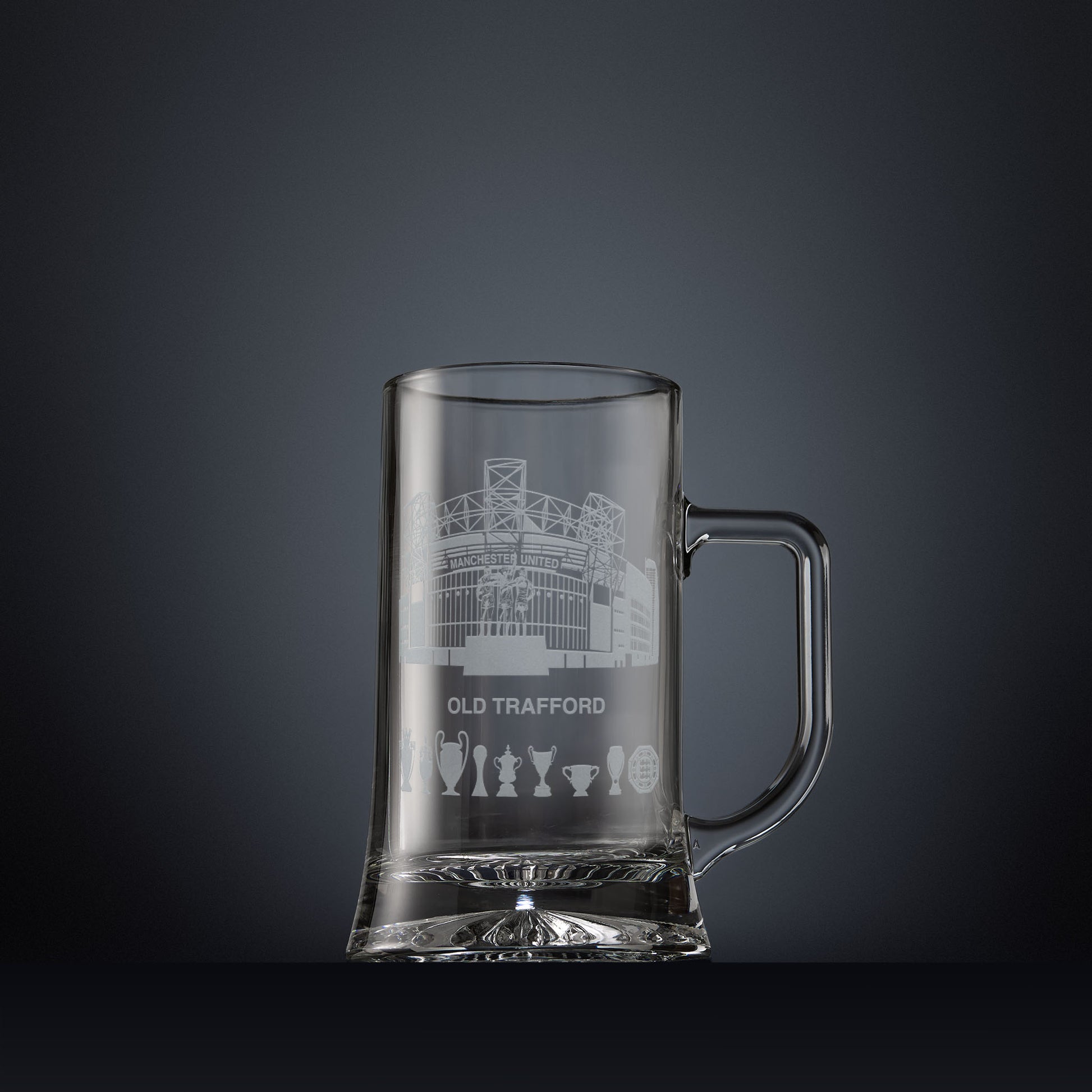 Glass tankard engraved with a line-art interpretation of Old Trafford stadium, with football trophy silhouettes beneath, inspired by its distinctive architectural form.