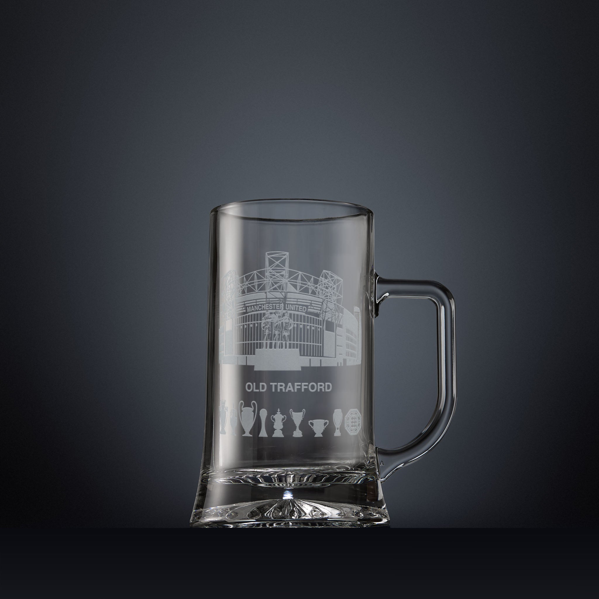 Glass tankard engraved with a line-art interpretation of Old Trafford stadium, with football trophy silhouettes beneath, inspired by its distinctive architectural form.