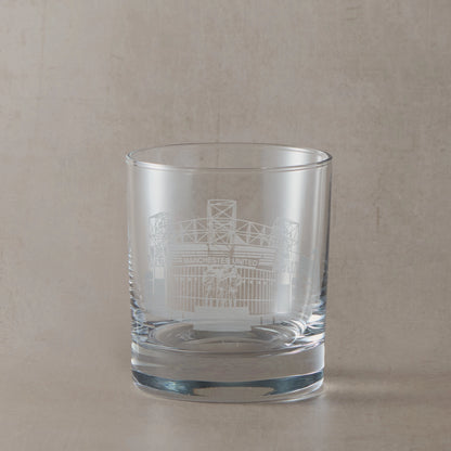 Whisky glass engraved with the facade of Old Trafford stadium, on a beige backround