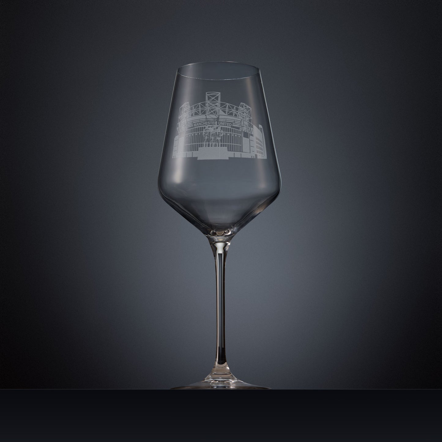Engraved wine glass featuring a line-art illustration of Old Trafford stadium, shown on a dark background