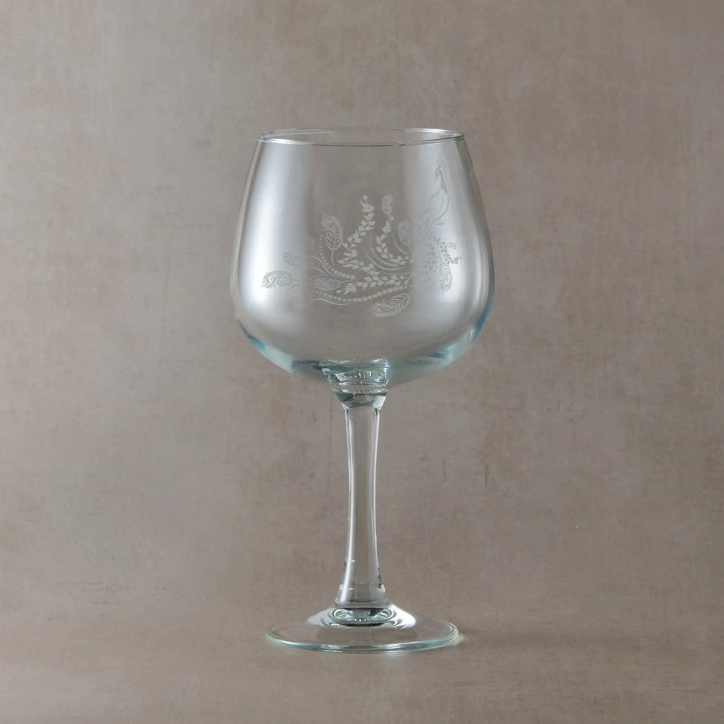 Engraved gin glass featuring a flowing peacock with feathers and trailing leaves, inspired by Pittencrieff Park’s flora