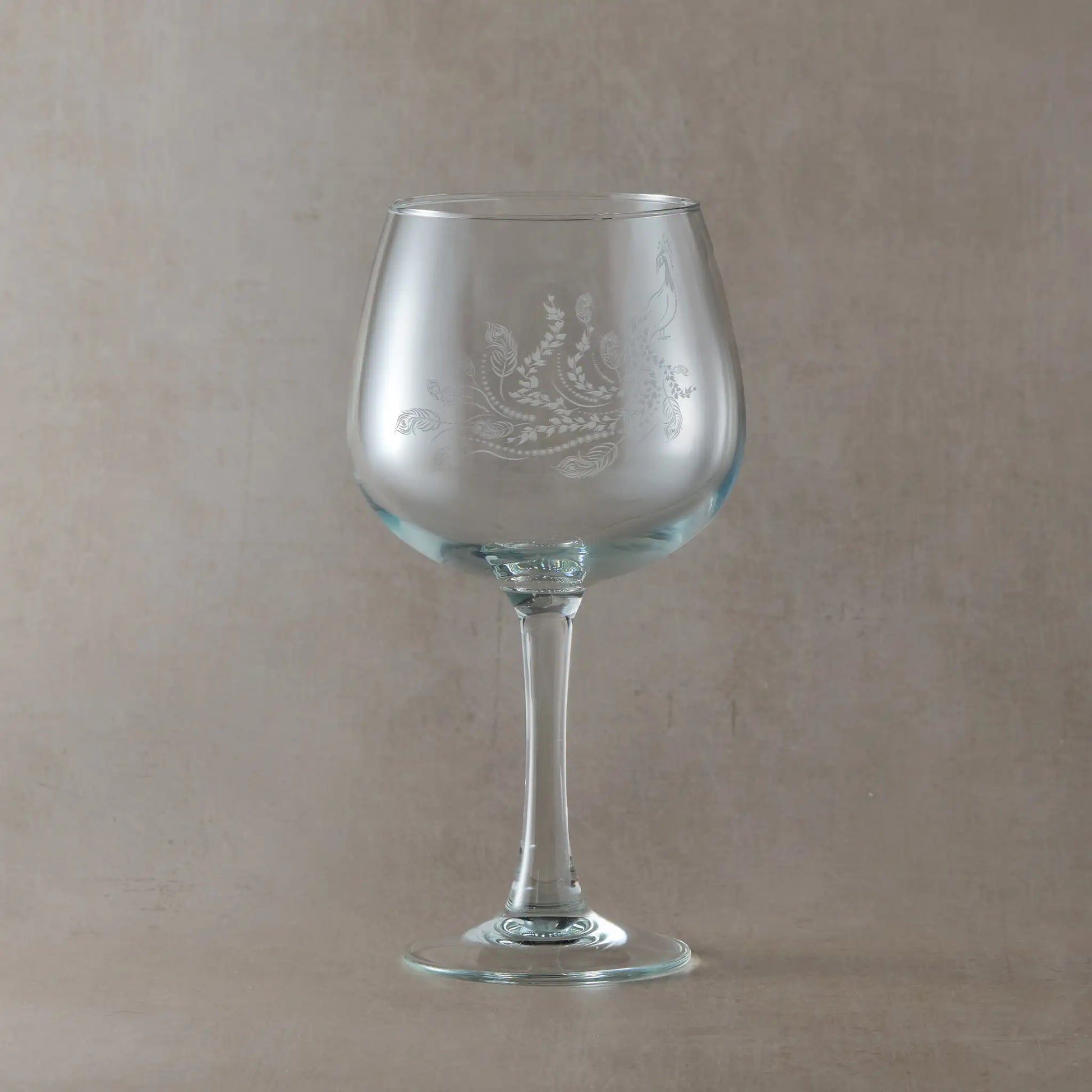 Engraved gin glass featuring a flowing peacock with feathers and trailing leaves, inspired by Pittencrieff Park’s flora