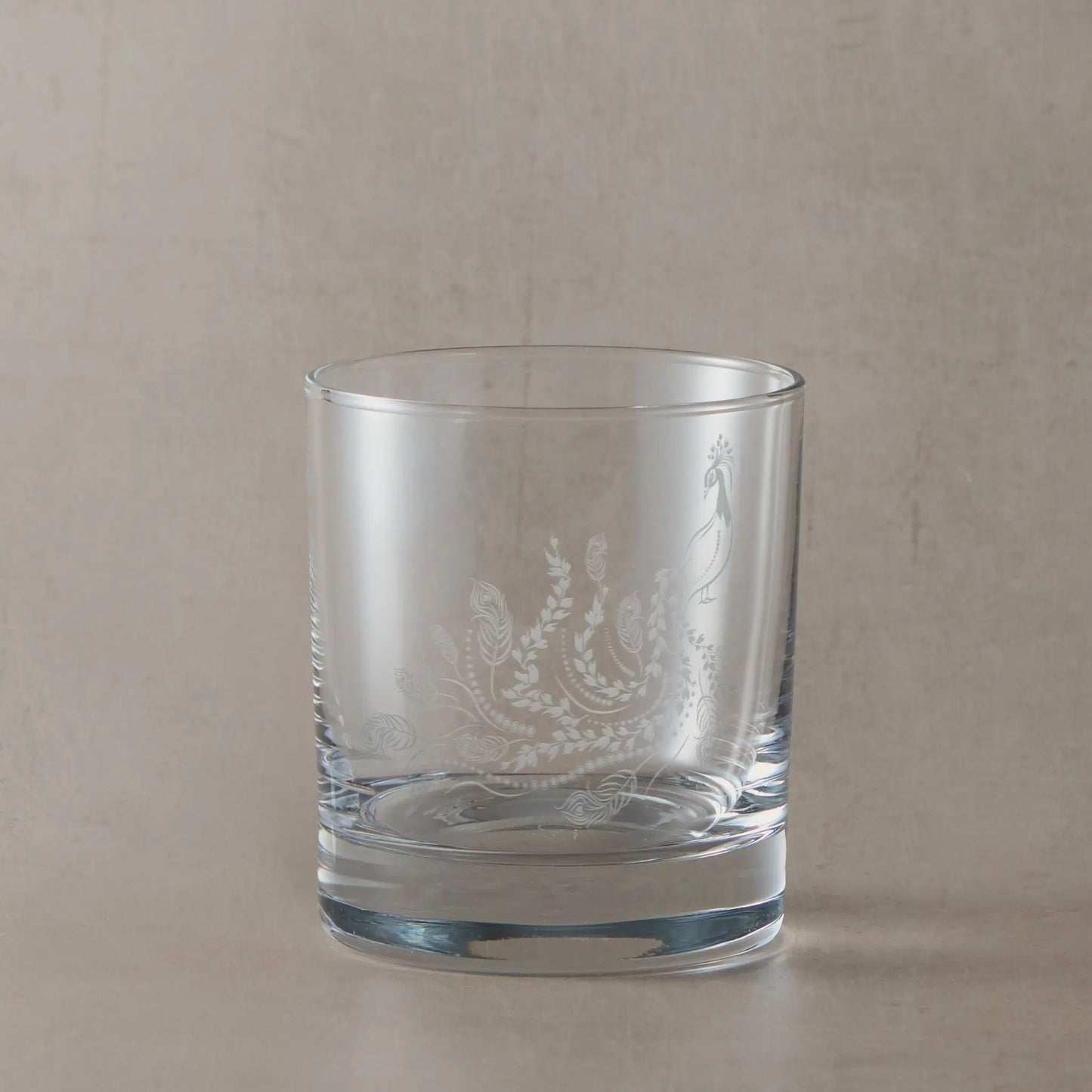 Engraved peacock on a whisky glass placed on a wooden surface with a bottle of Daftmill whisky in the background.