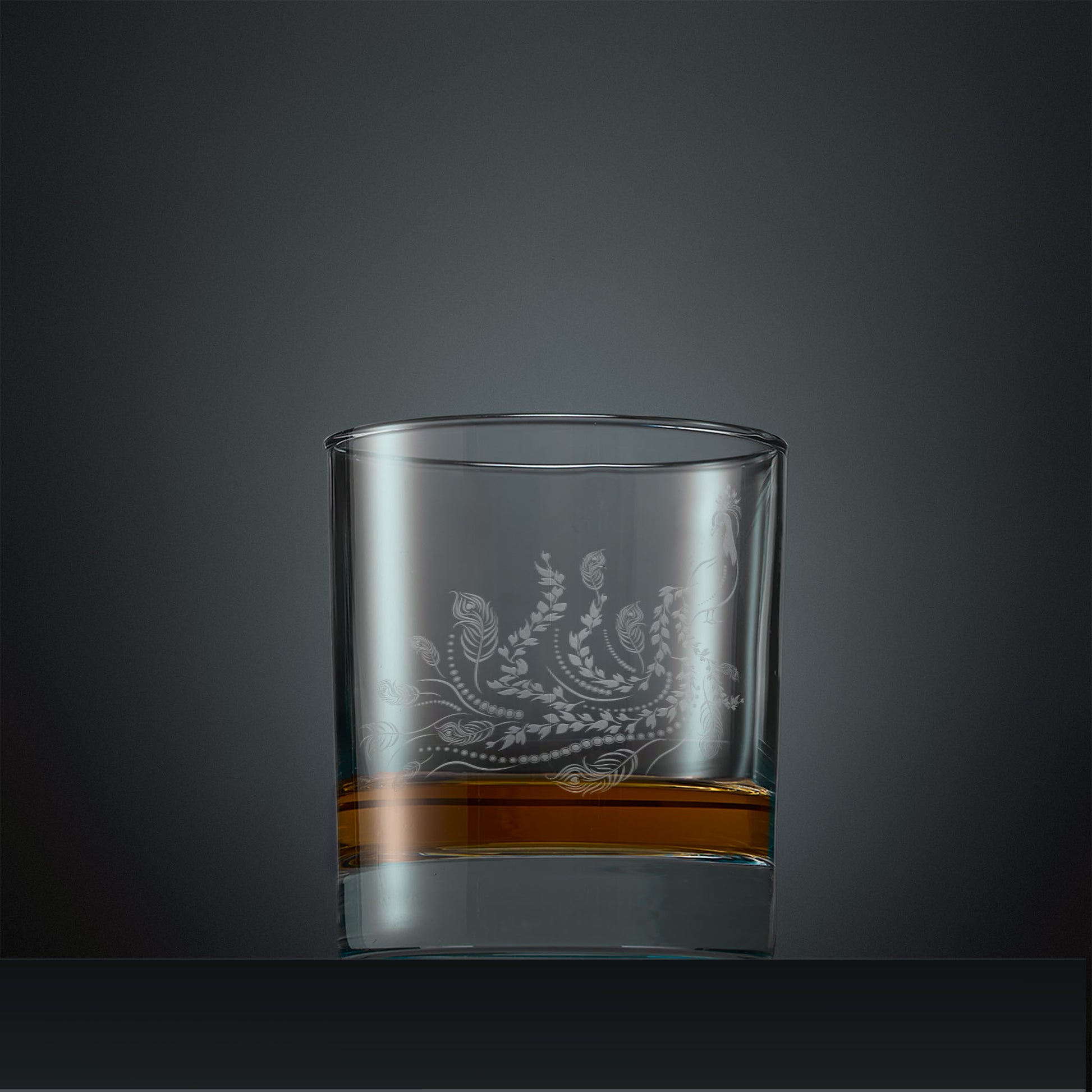 Engraved whisky glass with a peacock, trailing leaves and feathers design