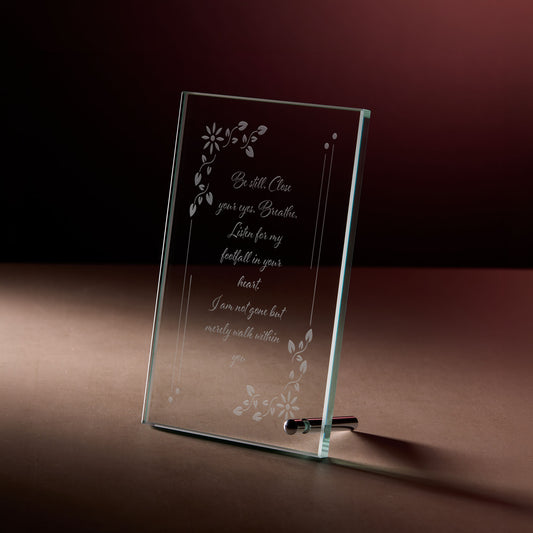 Glass memorial plaque with engraved text and floral designs on a dark background