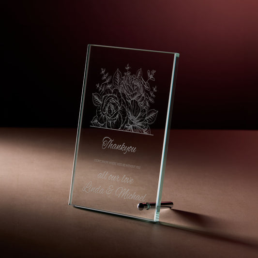 Glass display plaque with engraved flowers and thank you message photographed on a dark, softly lit background