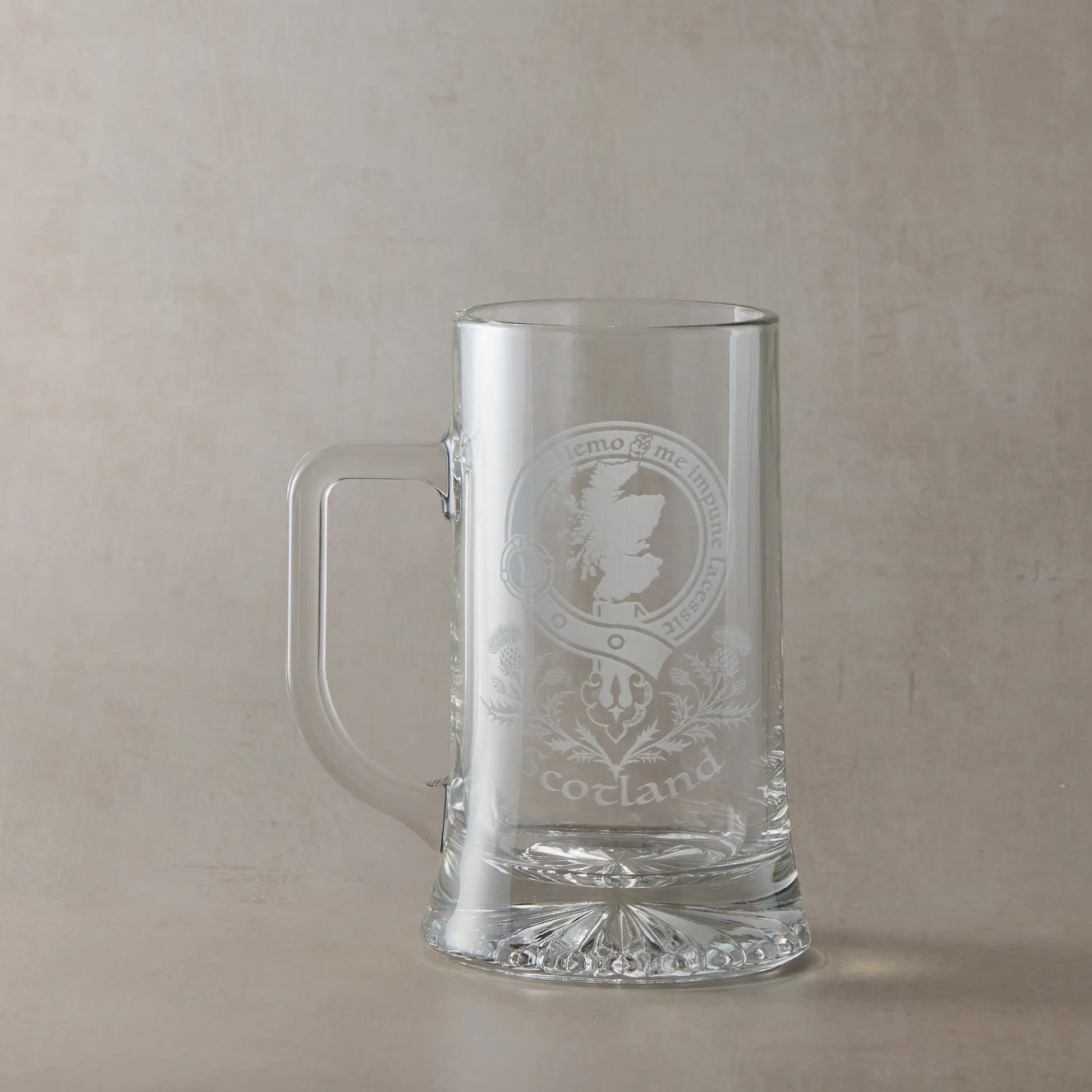 Clear glass beer tankard with engraved Scotland map crest design on a beige background