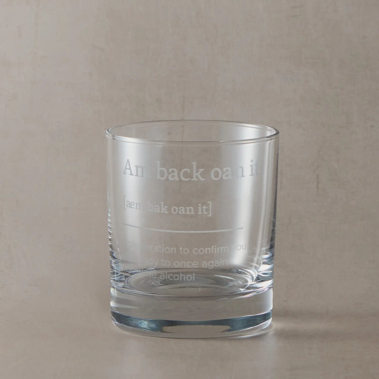 Whisky glass engraved with the Scottish phrase “Am Back Oan It” on a black background.