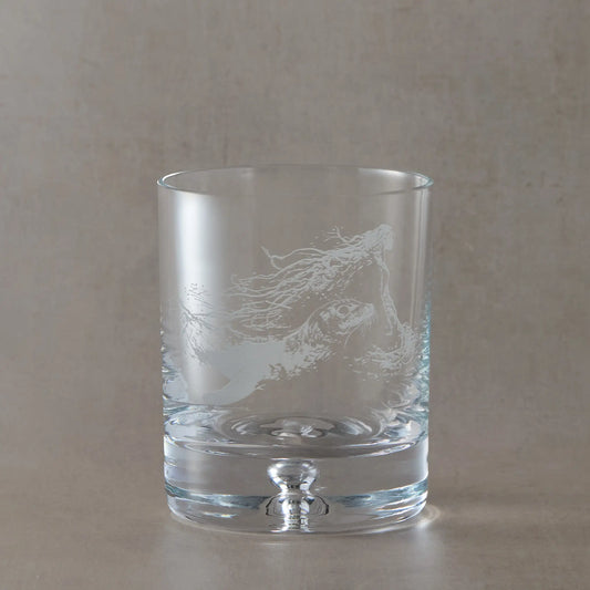 Engraved whisky glass featuring a selkie emerging with a seal, with flowing hair and ocean movement, photographed on a soft neutral background