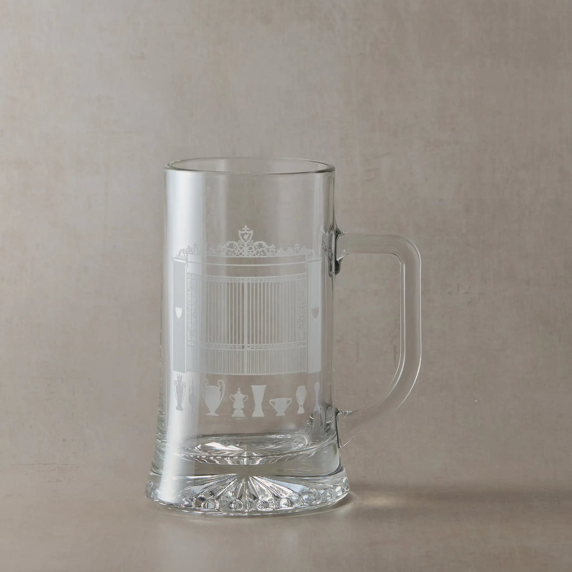 Tankard engraved withof Anfield's Shankly Gates with football trophy silhouettes, photographed on a beige background.