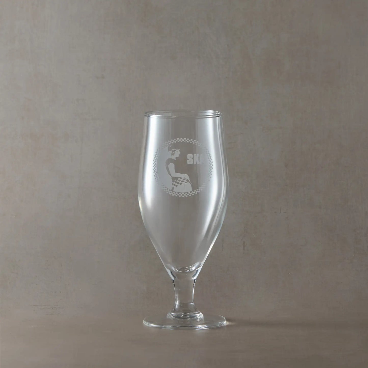 Stemmed eer glass engraved with SKA rude girl surrounded by a checkerboard design, shown on a beige background