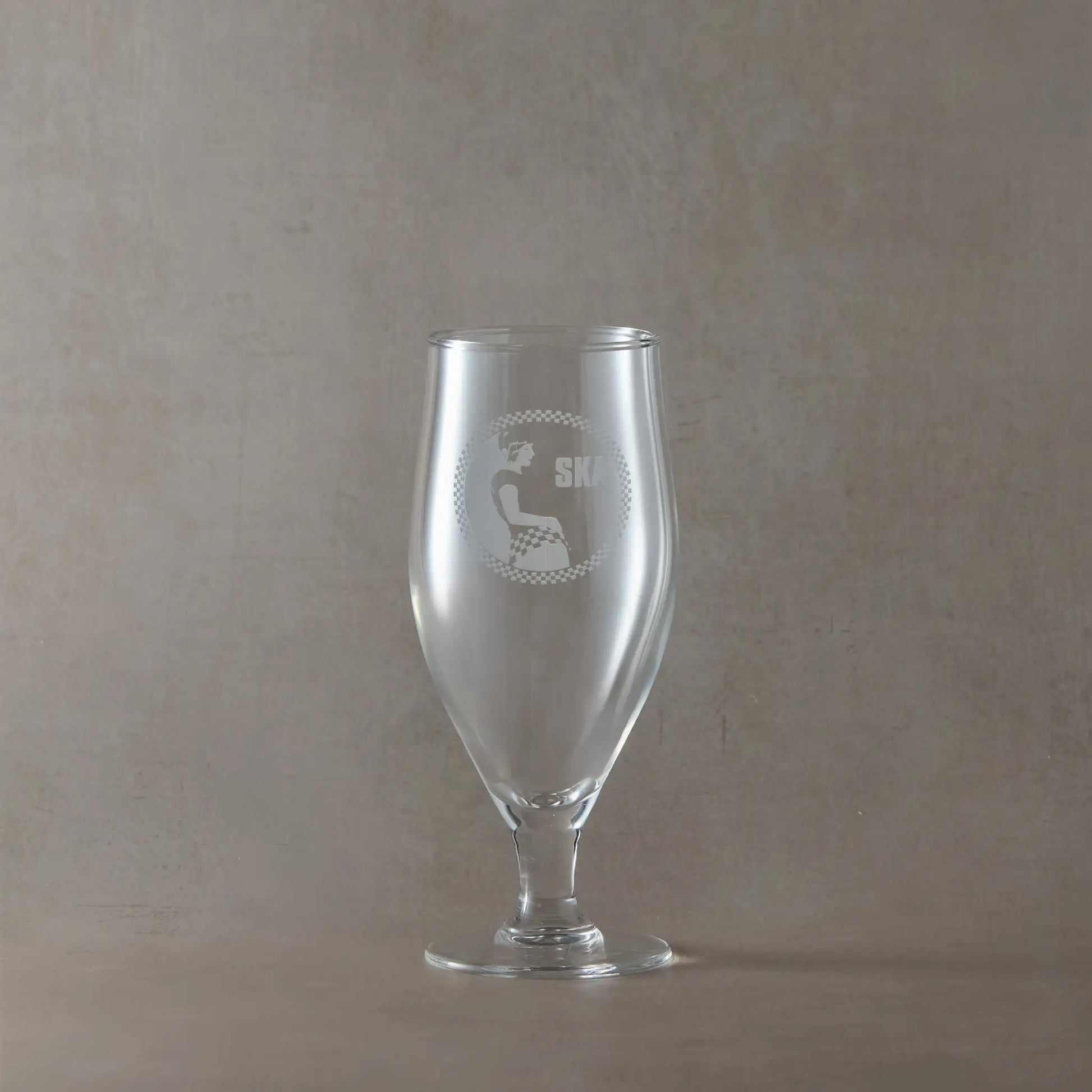 Stemmed eer glass engraved with SKA rude girl surrounded by a checkerboard design, shown on a beige background