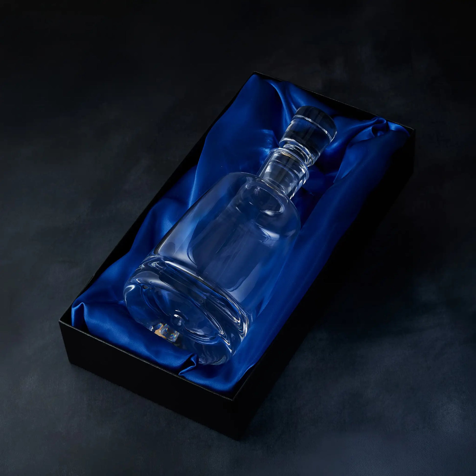 Handmade glass spirit decanter on blue satin fabric in a black presentation box against a dark background