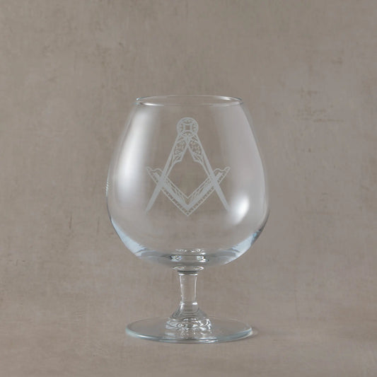 Brandy glass with Masonic square and compass symbol on a beige background