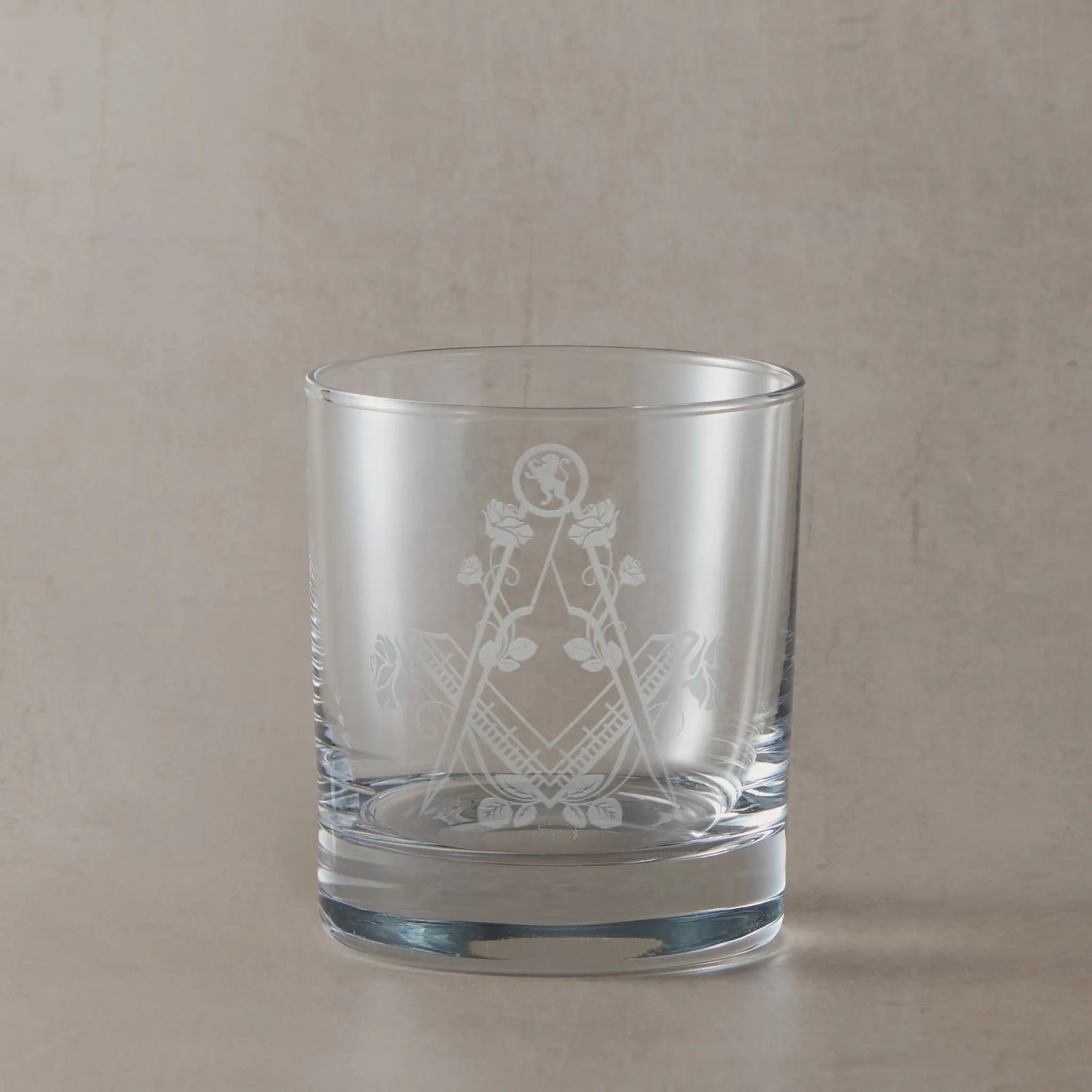 Masonic whiskey glass with Square & Compass, Lion rampant, and roses on a beige background