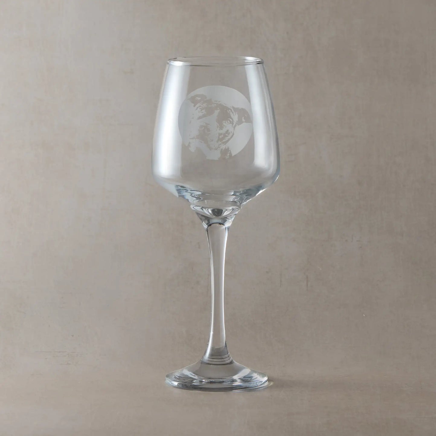 Wine glass engraved with a portrait of a Staffordshire Bull Terrier shown against a beige background.