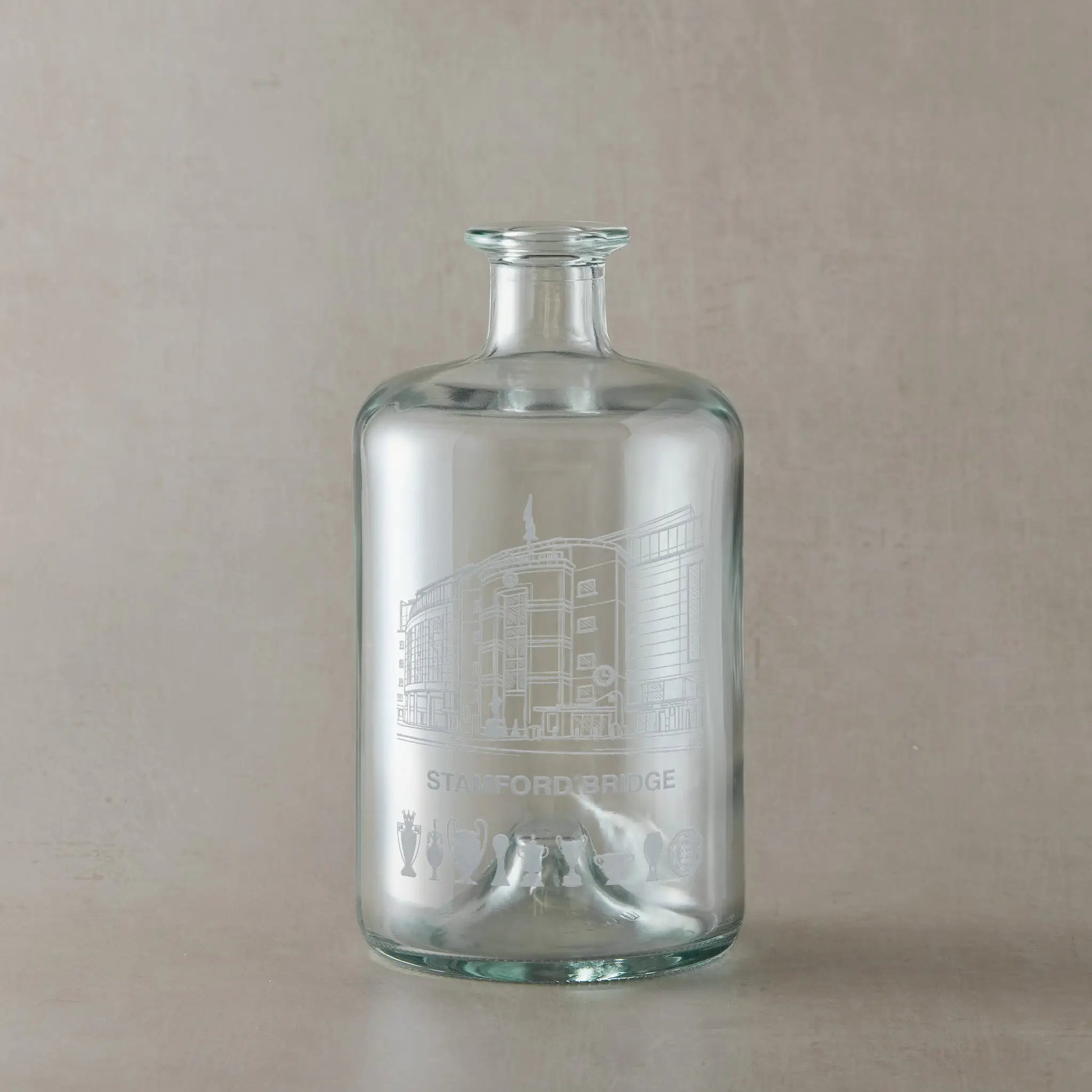 Clear glass bottle with engraved Stamford Bridge design on a beige background