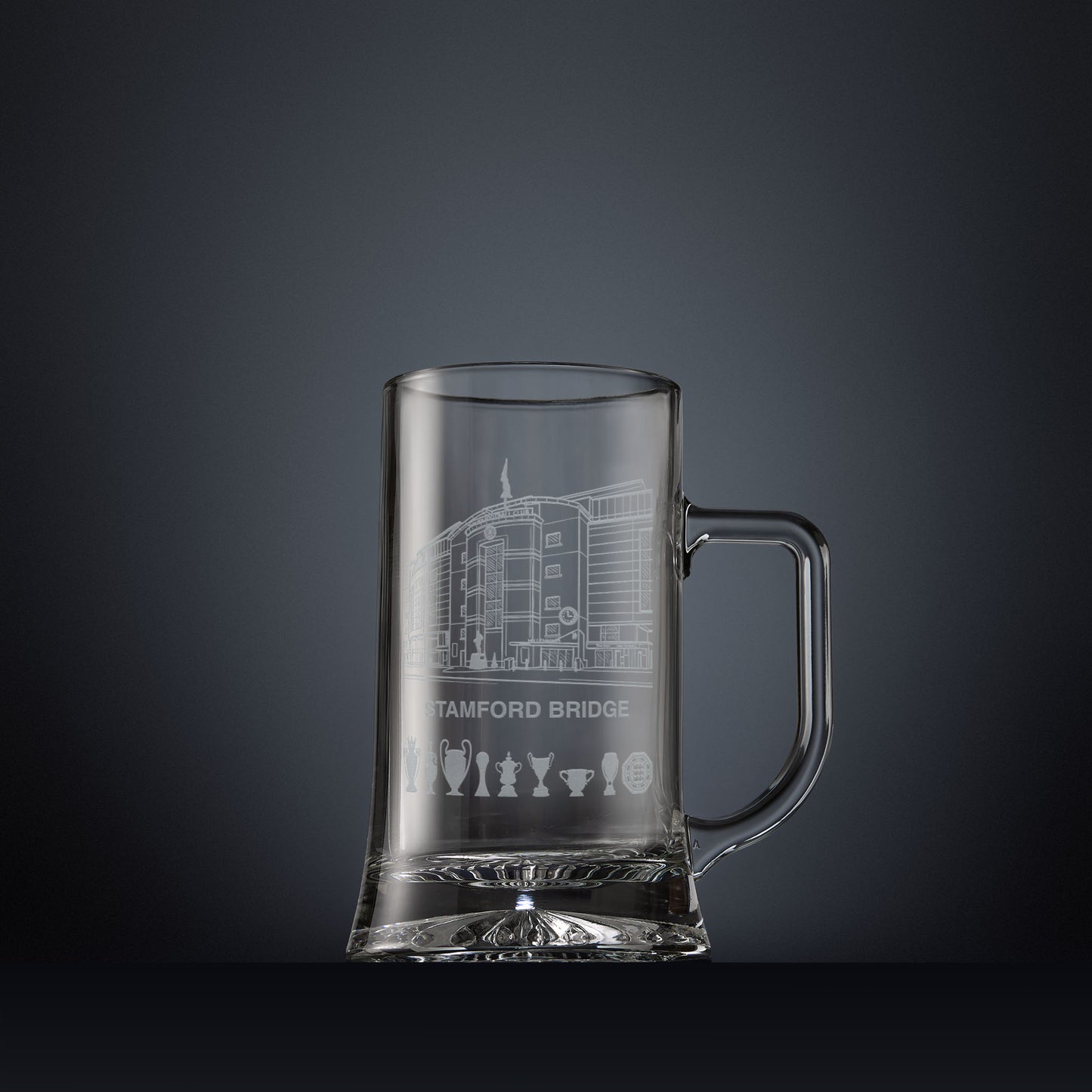 Engraved Stamford Bridge football stadium tankard shown on a dark panelled background with trophy silhouettes.