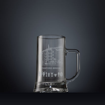 Engraved Stamford Bridge football stadium tankard shown on a dark panelled background with trophy silhouettes.