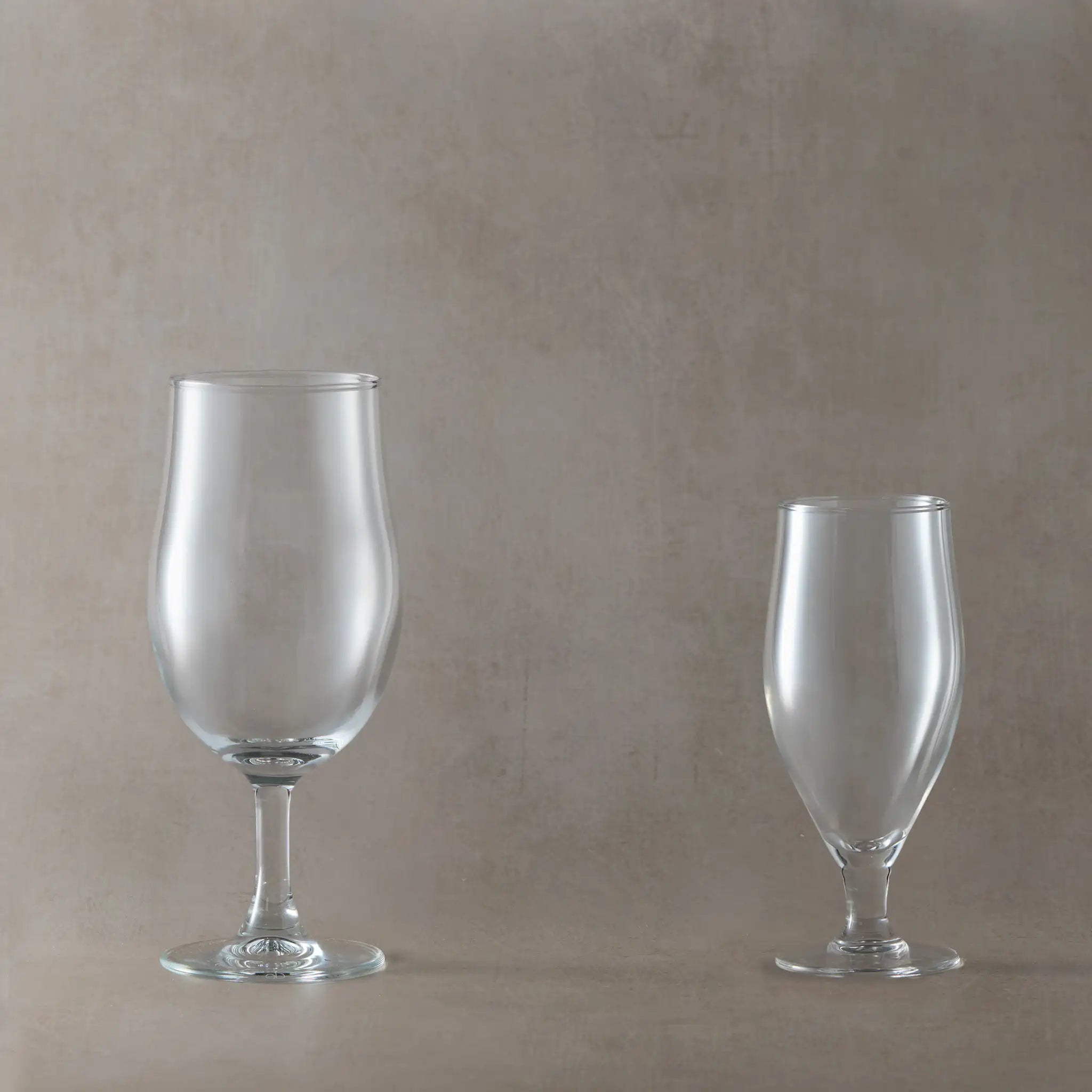 Two clear stemmed beer glasses on a beige background
