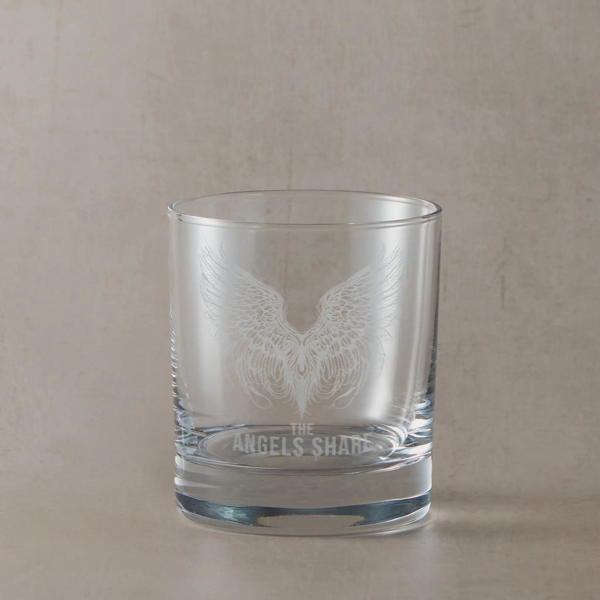 Clear whisky glass engraved with detailed angel wings and “The Angel’s Share” text, photographed on a soft neutral background