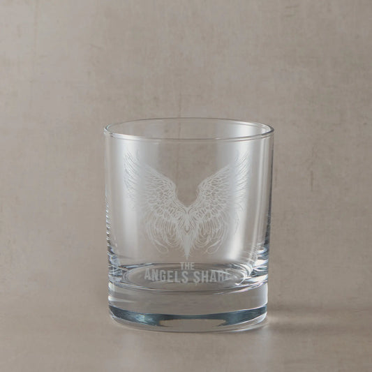 Clear whisky glass engraved with detailed angel wings and “The Angel’s Share” text, photographed on a soft neutral background