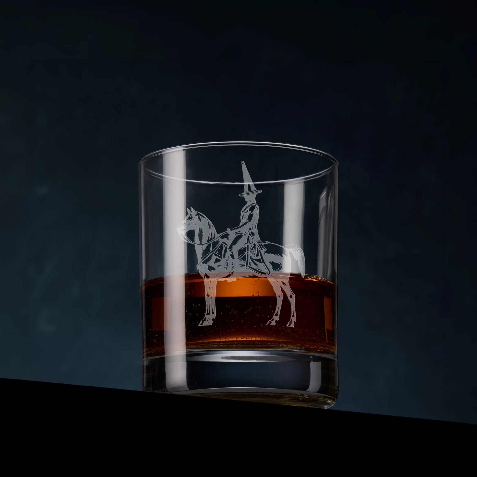 Engraved whisky glass featuring the Duke of Wellington statue in Glasgow, complete with its iconic traffic cone, shown on a dark studio background with a dram of whisky to highlight the engraving