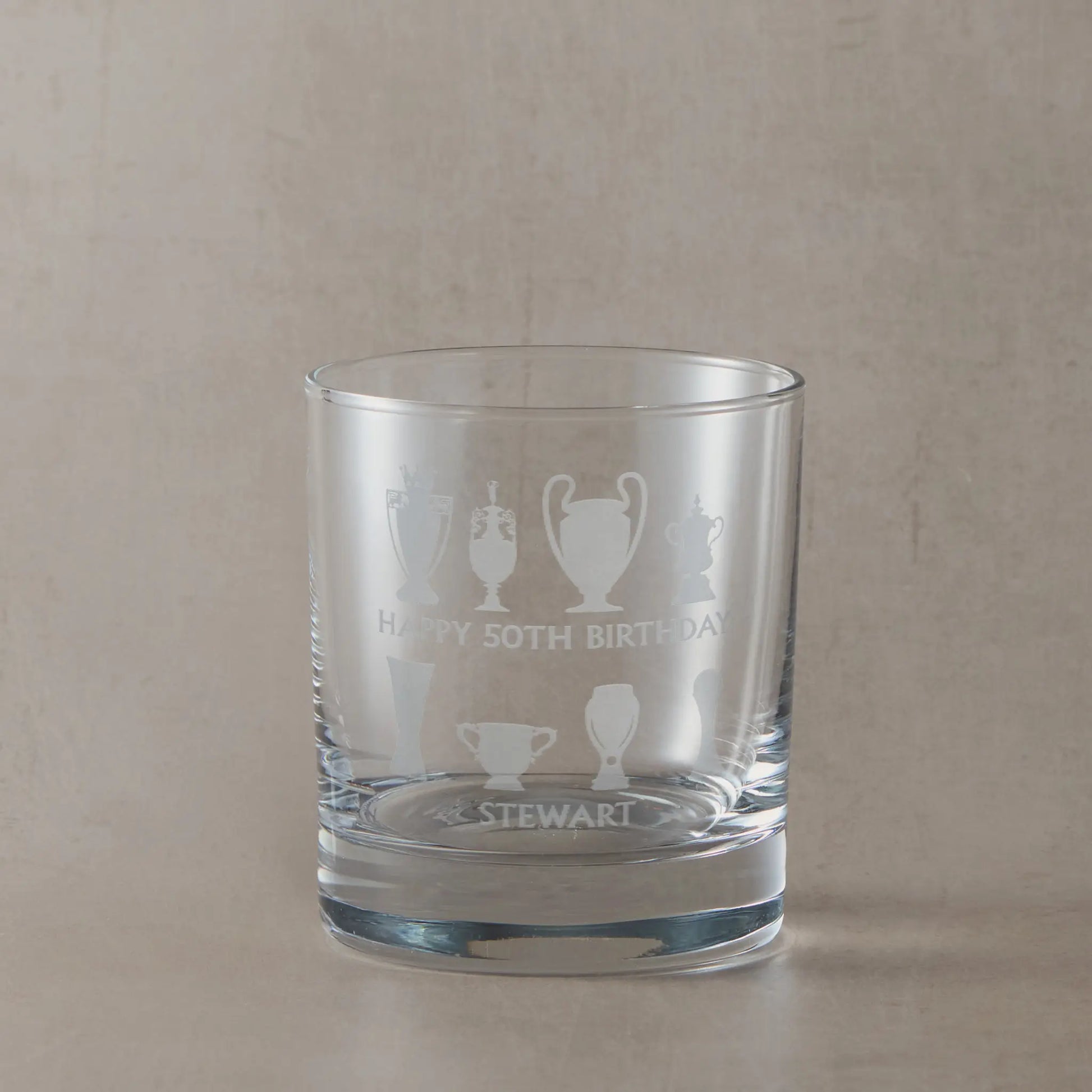 Personalised whisky glass engraved with honours wall trophy silhouettes photographed on a beige background