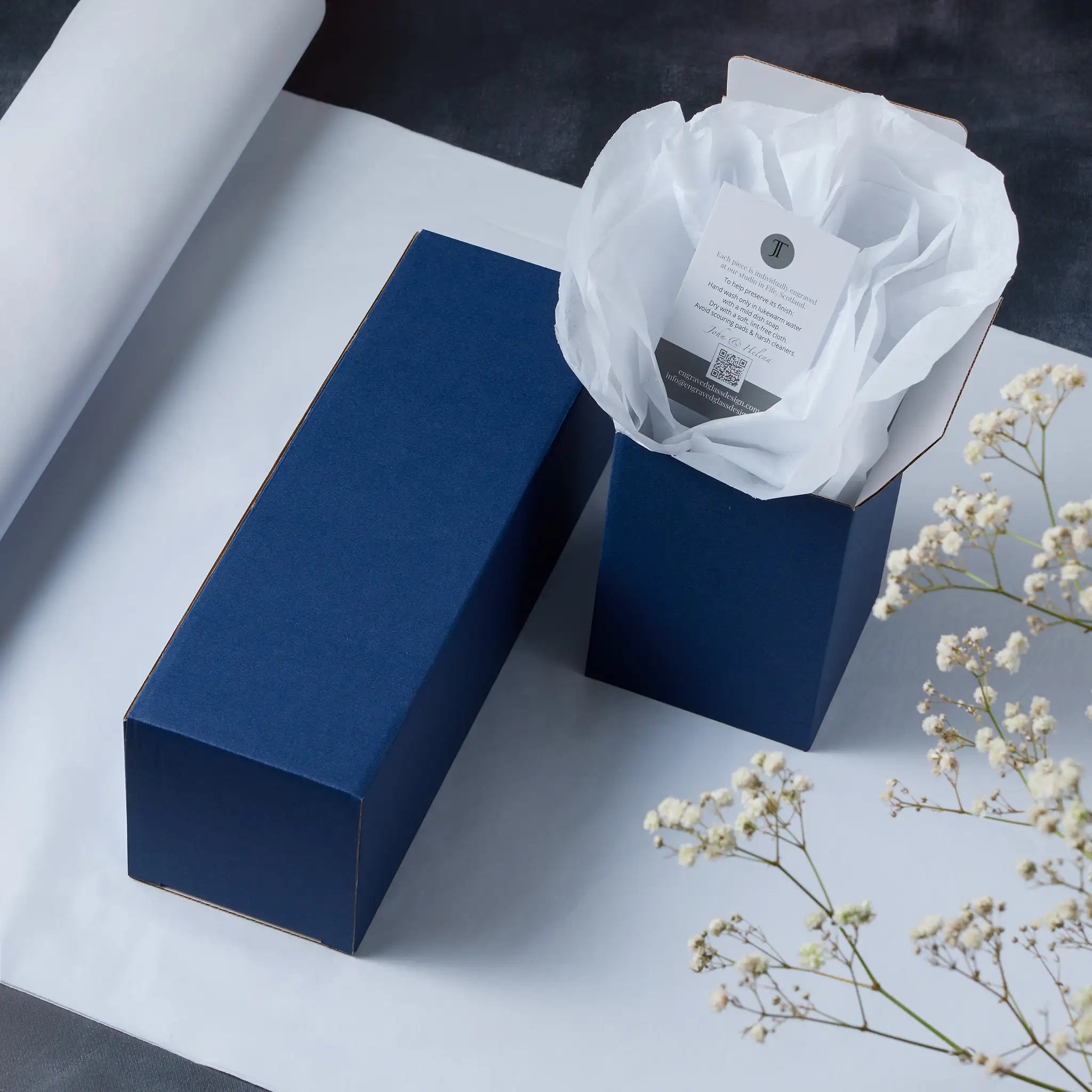 Blue gift box with tissue paper on a light surface with white flowers.