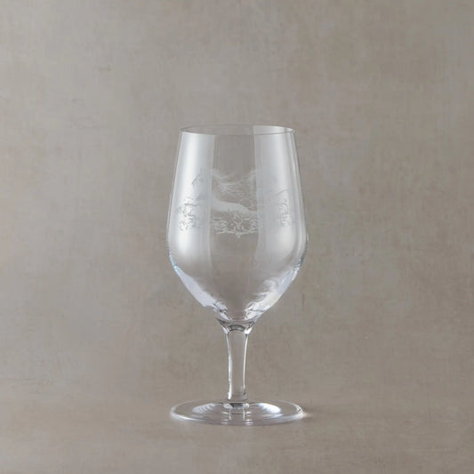 Clear mineral water glass with engraved horse design on a beige background