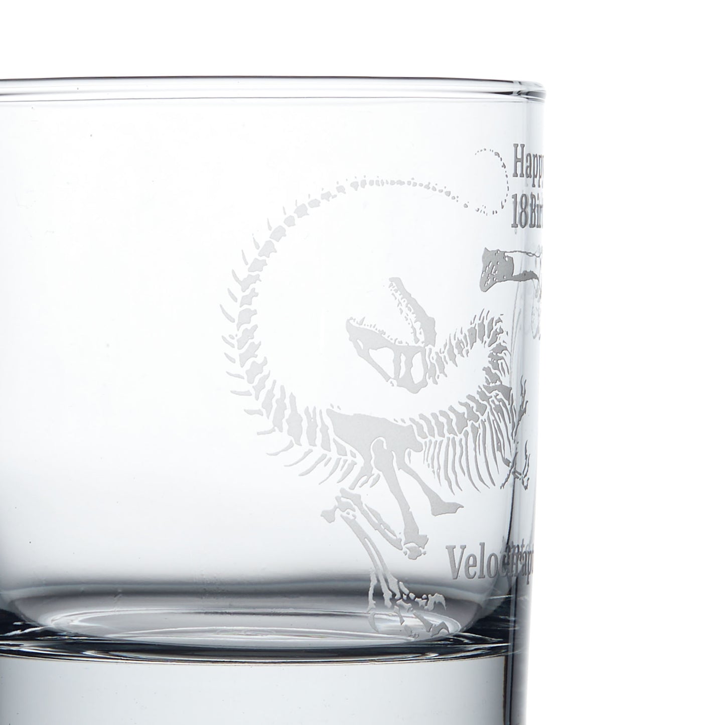 Close-up detail of a personalised whisky glass engraved with a Velociraptor dinosaur fossil