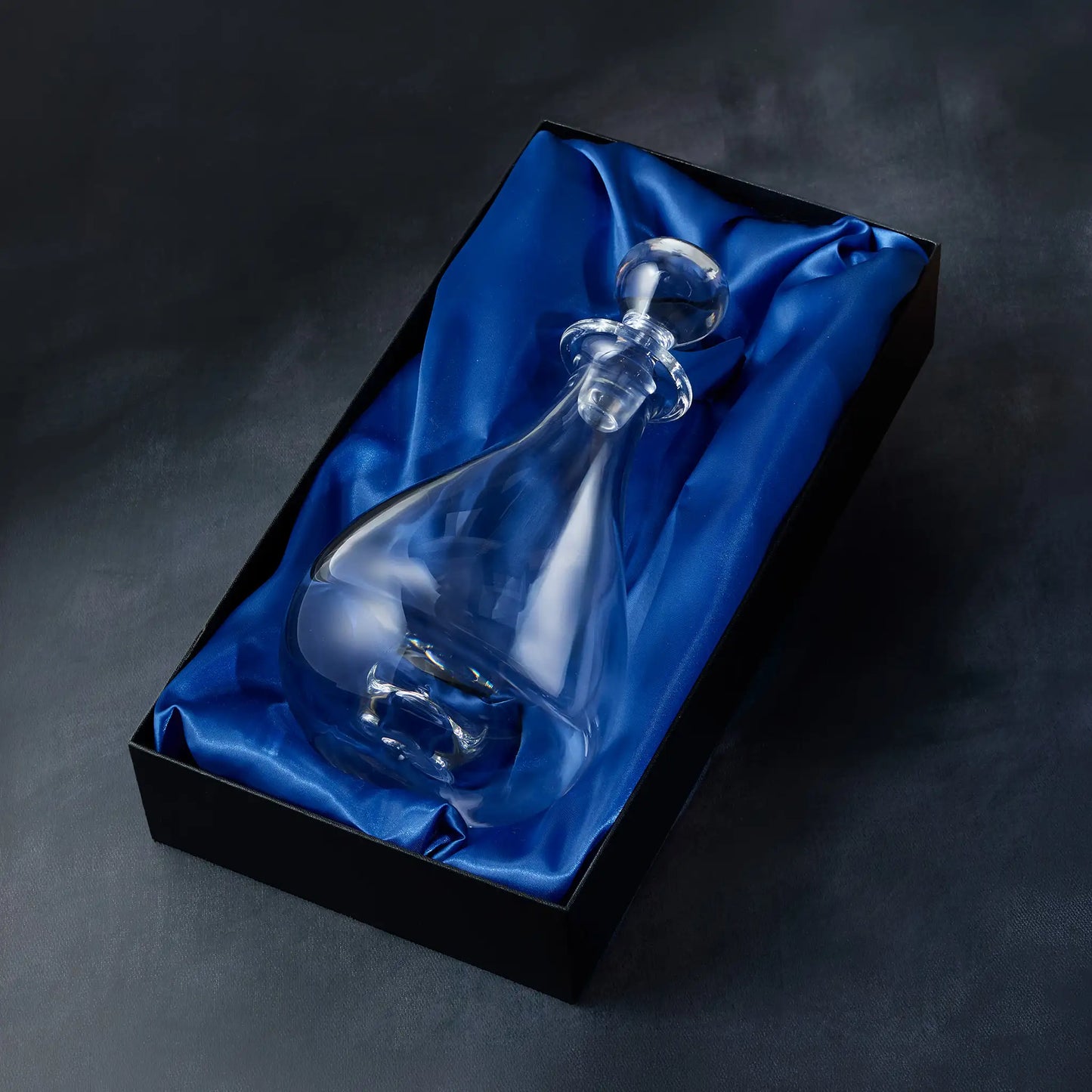 Handmade glass wine decanter on blue satin fabric in a black presentation box against a dark background
